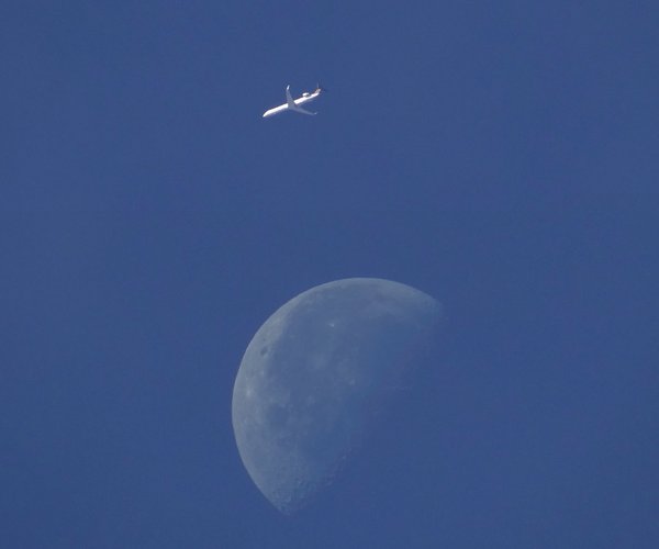 Taken with midday sun shining the moon is rather pale. Aircraft is a CRJ 900 of Eurowings.
